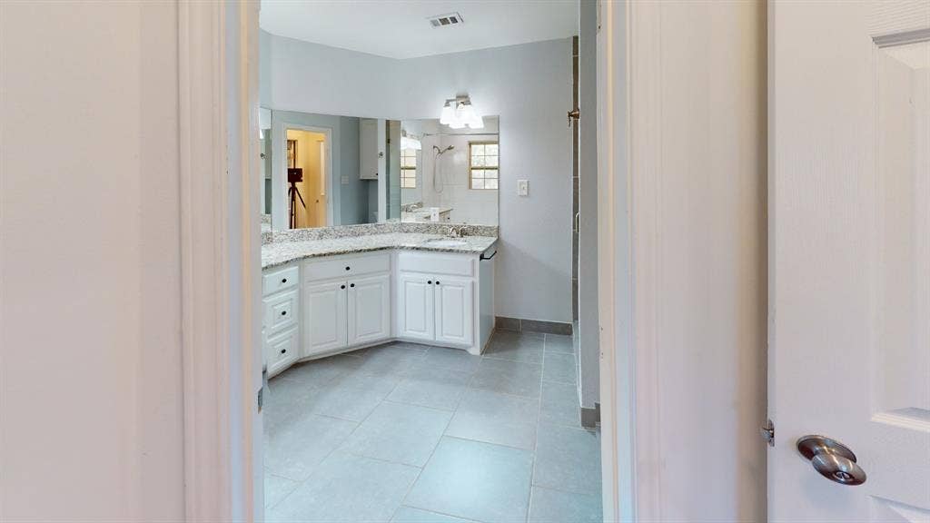Dual vanity with white cabinetry, granite-style countertop, and expansive wall-mounted mirror