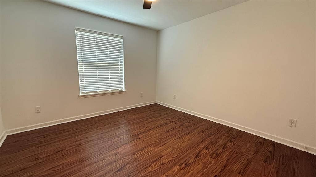 Spacious room featuring wood-finish flooring, a window with blinds, and a ceiling fan