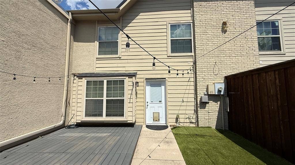 Exterior featuring horizontal siding, brick accents, a ground-level deck, a concrete walkway, and a fenced yard with artificial turf