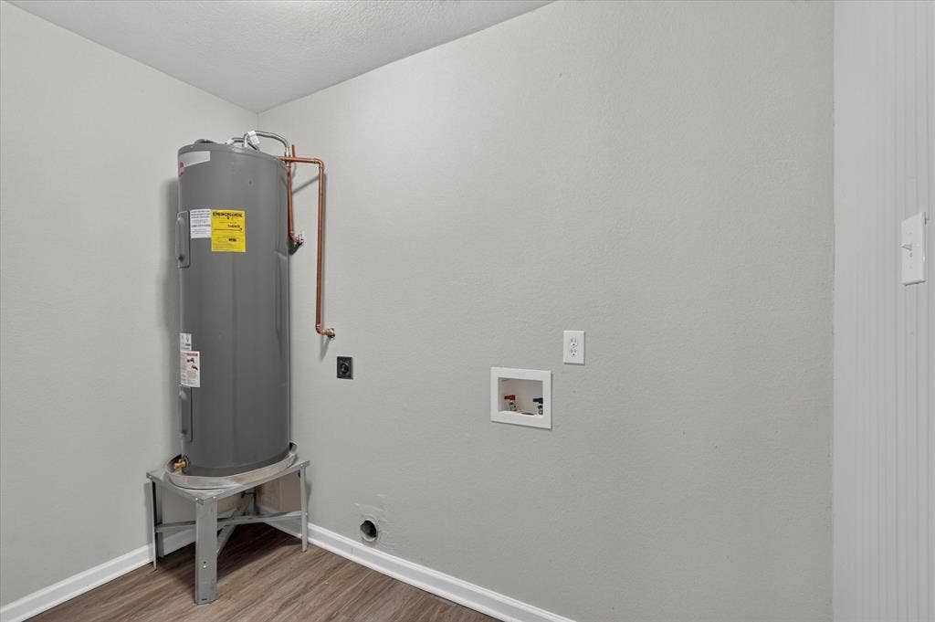 201 West Lane, West Tawakoni, TX 75474 Dedicated utility space with a water heater, laundry hookups, and wood-finish flooring