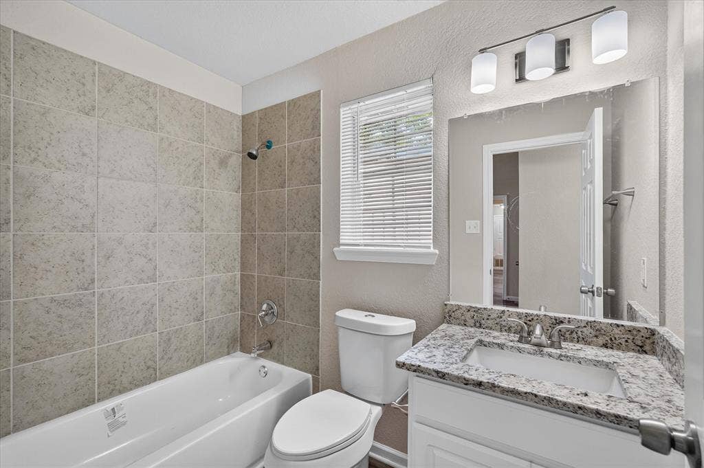 201 West Lane, West Tawakoni, TX 75474 Bathroom featuring a tiled shower surround, white bathtub, vanity with a stone countertop, and an overhead light fixture