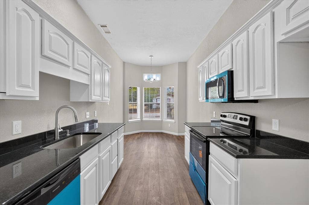 201 West Lane, West Tawakoni, TX 75474 Kitchen featuring white cabinetry, dark countertops, stainless steel sink, wood-finish flooring, and bay windows
