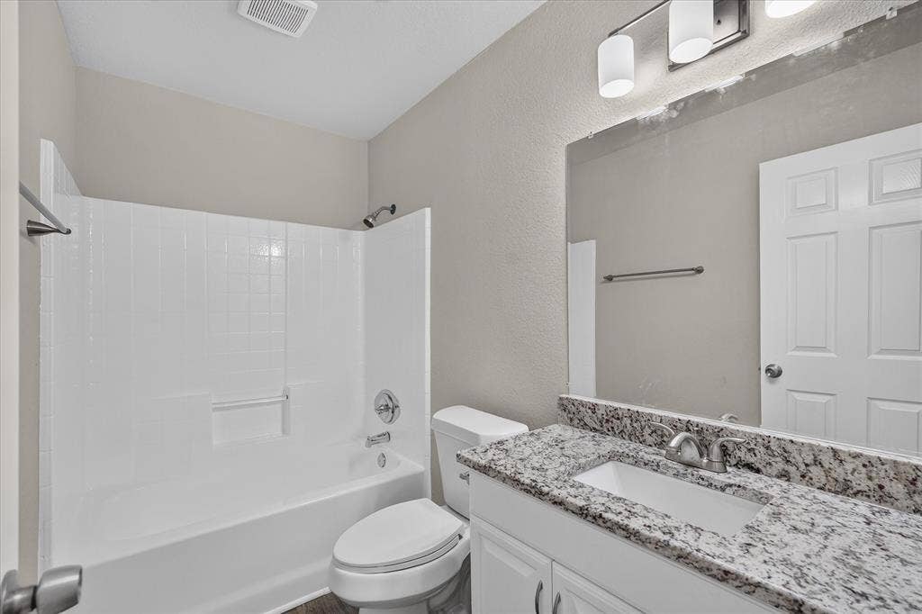 201 West Lane, West Tawakoni, TX 75474 Tub and shower combination with chrome fixtures, vanity with a speckled countertop, and built-in white cabinetry