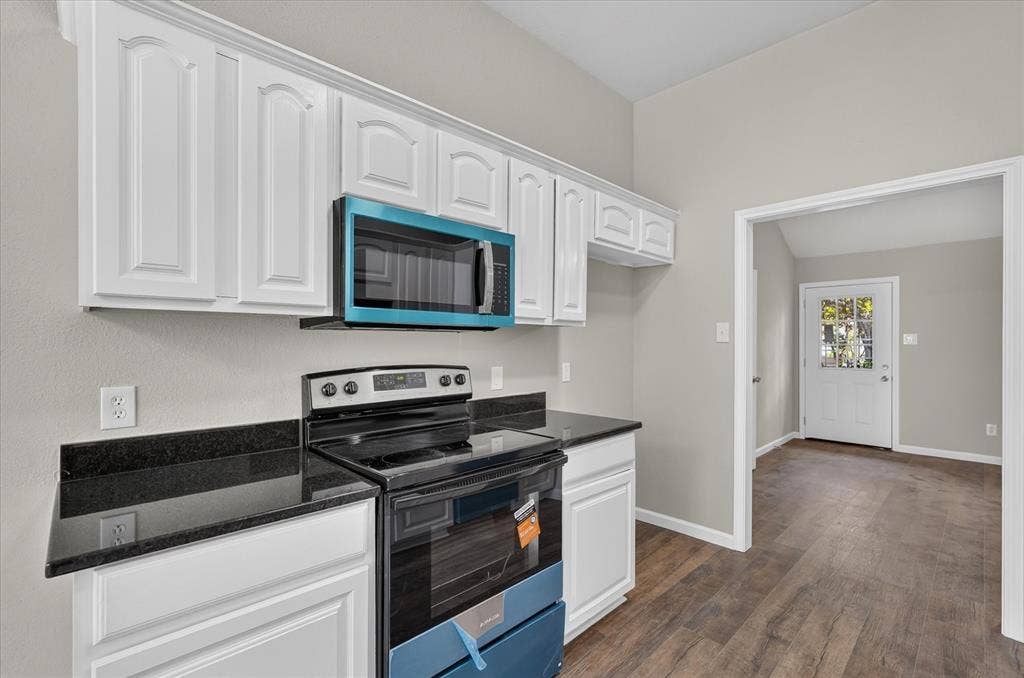 201 West Lane, West Tawakoni, TX 75474 White cabinetry, dark countertops, wood-finish flooring, and a vaulted ceiling