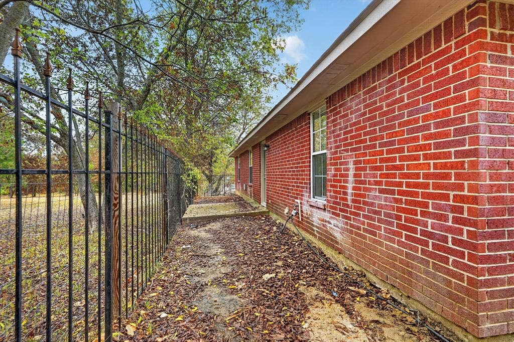 201 West Lane, West Tawakoni, TX 75474 Red brick exterior with white trim, featuring a single window and an ornamental black metal fence