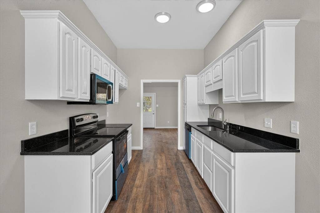 201 West Lane, West Tawakoni, TX 75474 White cabinetry with crown molding, black countertops, stainless steel sink with gooseneck faucet, microwave, and wood-finish flooring