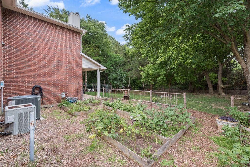 Raised garden beds and mature trees create a peaceful backyard setting with plenty of space to garden, relax, and enjoy the outdoors.