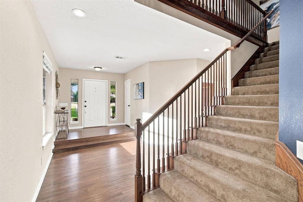 Step inside to a bright entryway with rich wood-look flooring, an elegant paneled front door with sidelights, and a staircase with a warm wood handrail.