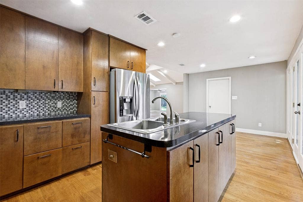 2937 Forest Hills Lane, Richardson, TX 75080 Kitchen featuring wood cabinetry, stainless steel appliances, a center island with sink, mosaic tile backsplash, and light wood-finish flooring