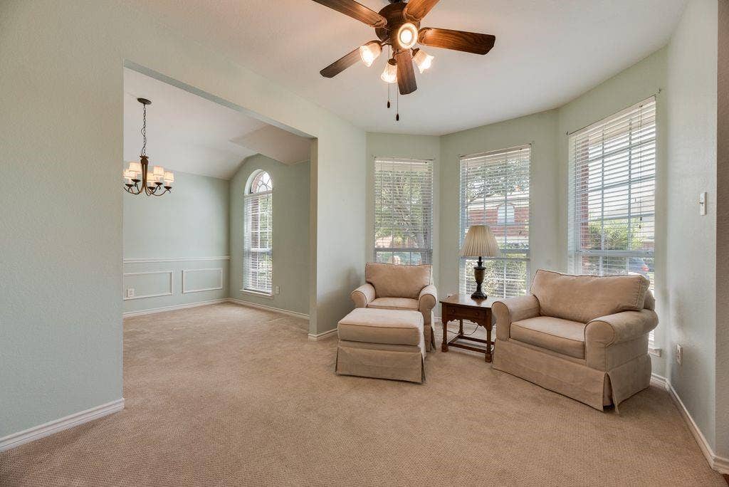 1485 Ashbourne Drive, Rockwall, TX 75087 Carpeted living area featuring a ceiling fan, bay windows with blinds, and an arched entry to a room with wainscoting and a chandelier