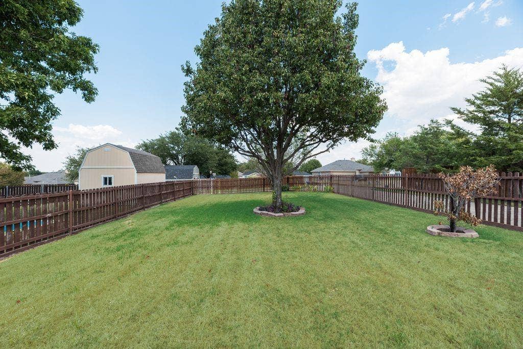 1485 Ashbourne Drive, Rockwall, TX 75087 Expansive green lawn with mature trees and a sturdy wood fence
