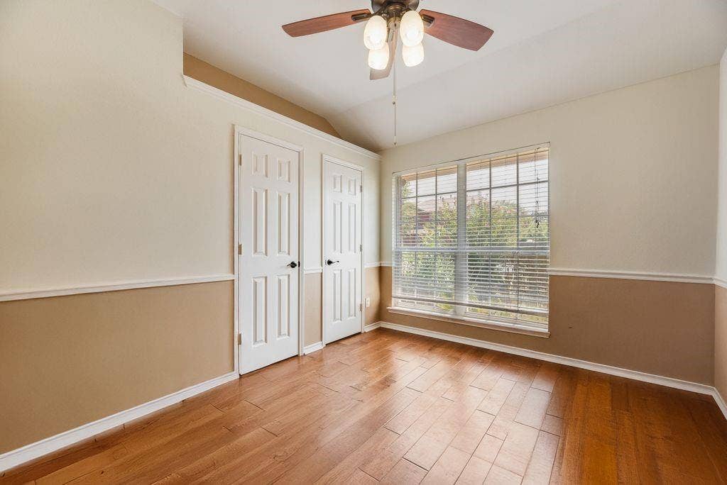 1485 Ashbourne Drive, Rockwall, TX 75087 Bedroom 2 Wood-finish flooring, two-tone wall treatment with chair rail, and a ceiling fan with integrated lighting