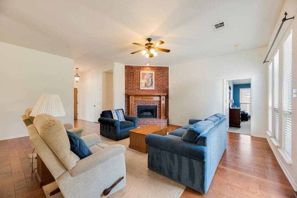 1485 Ashbourne Drive, Rockwall, TX 75087 Brick fireplace with wood mantle, wood-finish flooring, ceiling fan, and white window blinds