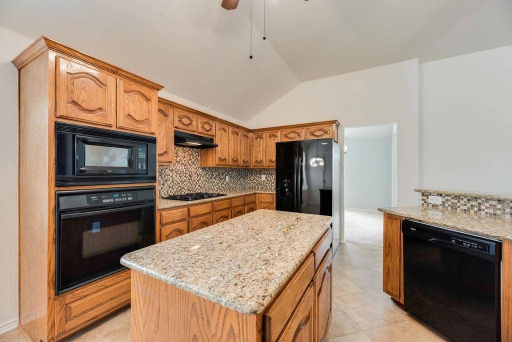 1485 Ashbourne Drive, Rockwall, TX 75087 Kitchen featuring wood cabinetry, granite-finish countertops, a tile backsplash, and integrated black appliances