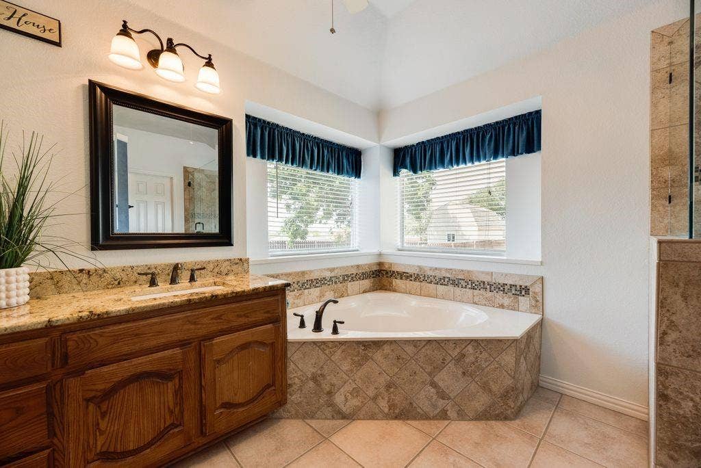 1485 Ashbourne Drive, Rockwall, TX 75087 Dual vanity with granite countertop, corner soaking tub with tile surround, tile flooring, and vaulted ceiling