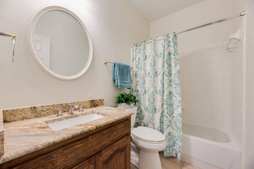 1485 Ashbourne Drive, Rockwall, TX 75087 Full Bathroom featuring a vanity with an integrated sink, a polished stone countertop, a circular framed mirror, and a tiled shower and tub