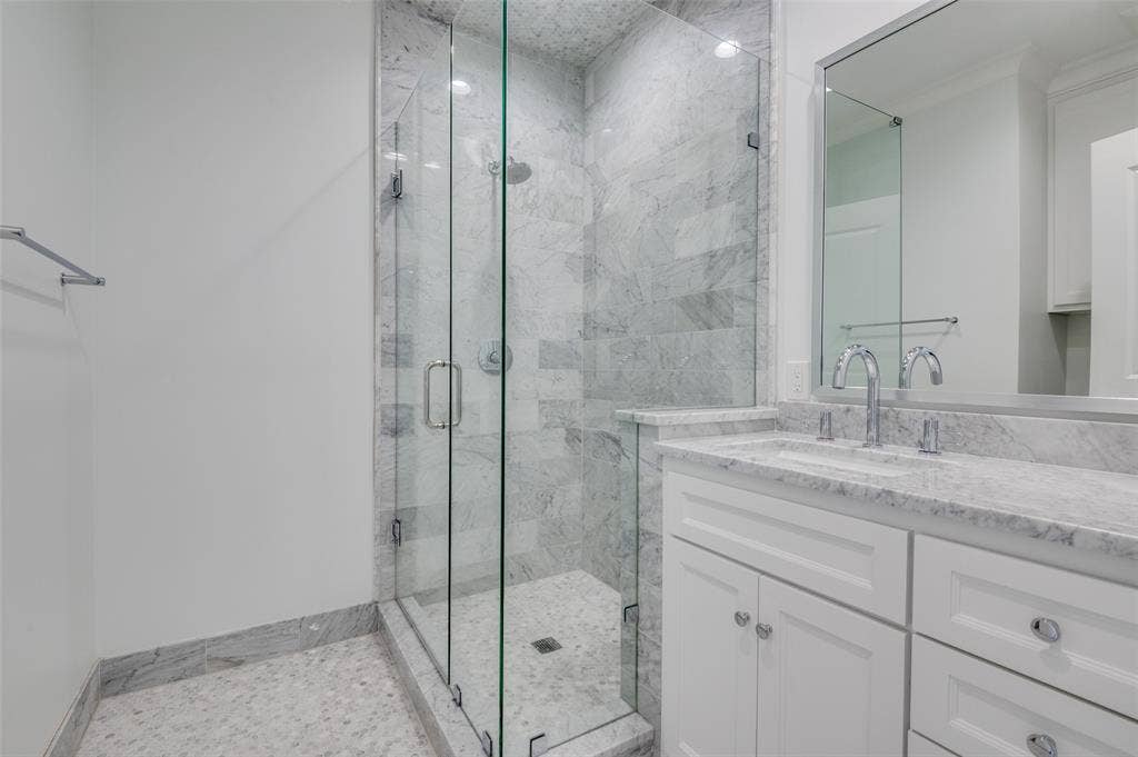 4031 Prescott Avenue, Dallas, TX 75219 Glass-enclosed shower with full-height tile surround, dual-handle shower fixtures, vanity with undermount sink, countertop, and framed mirror