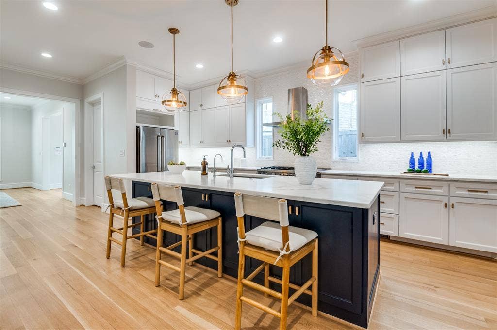4031 Prescott Avenue, Dallas, TX 75219 Spacious kitchen featuring an expansive center island with seating, stainless steel appliances, light-toned wood-finish flooring, white upper and lower cabinetry, and a tile backsplash