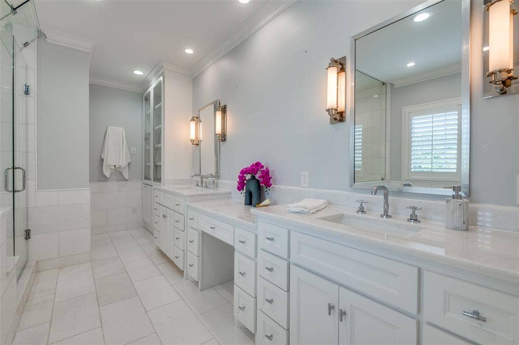 4031 Prescott Avenue, Dallas, TX 75219 Expansive bathroom featuring dual vanity sinks, extensive white cabinetry, a glass-enclosed shower, and built-in storage
