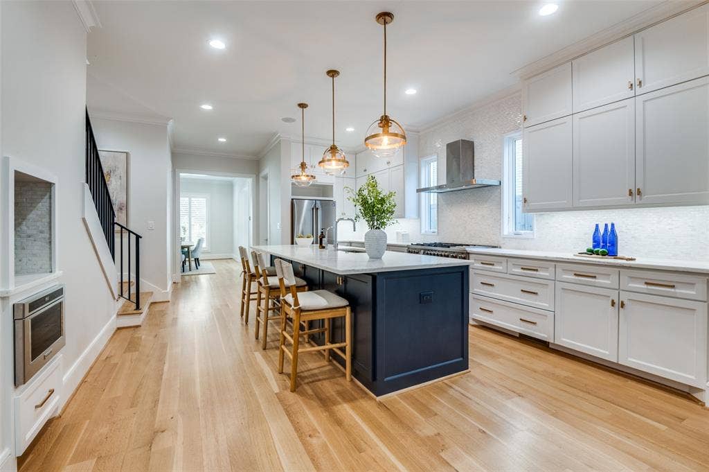 4031 Prescott Avenue, Dallas, TX 75219 Light wood-finish flooring, a kitchen island with a light-colored countertop, recessed lighting, white cabinetry, and stainless steel appliances