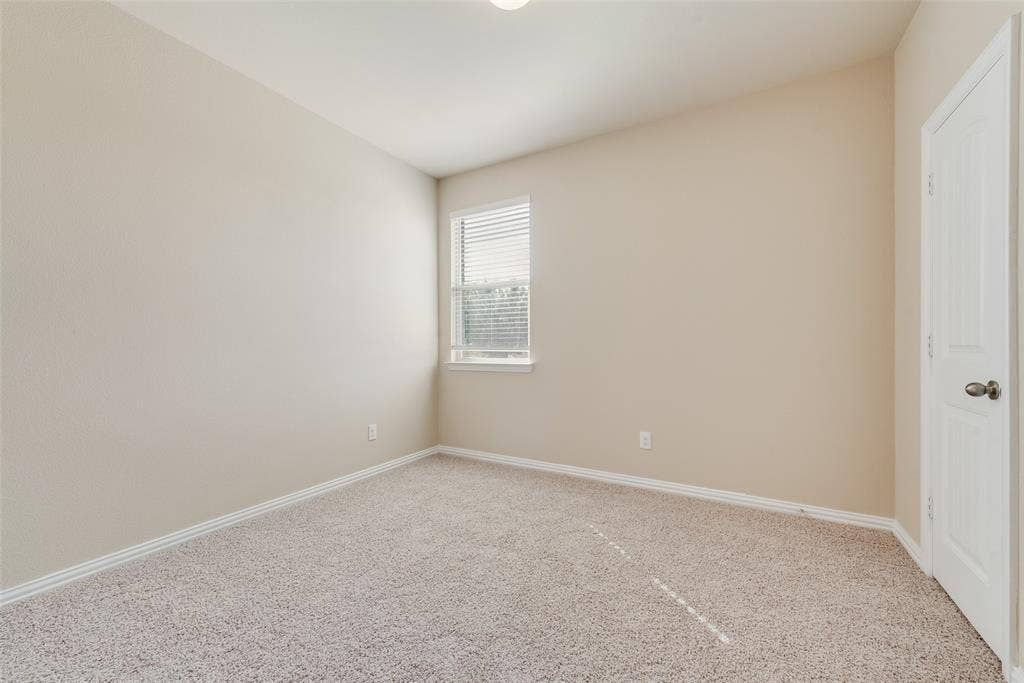 215 Fred Lane, Ferris, TX 75125 Neutral-toned walls, textured carpet flooring, a single window with blinds, and a white paneled door with a metallic knob