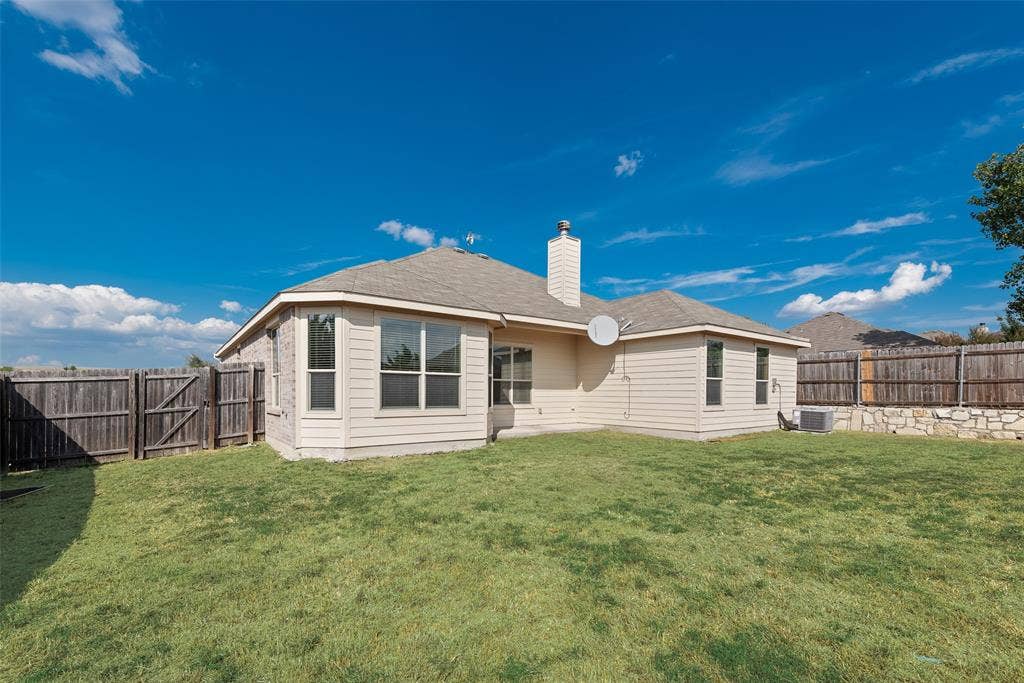 215 Fred Lane, Ferris, TX 75125 Expansive backyard featuring a wood privacy fence, stone retaining wall, and a multi-pane bay window