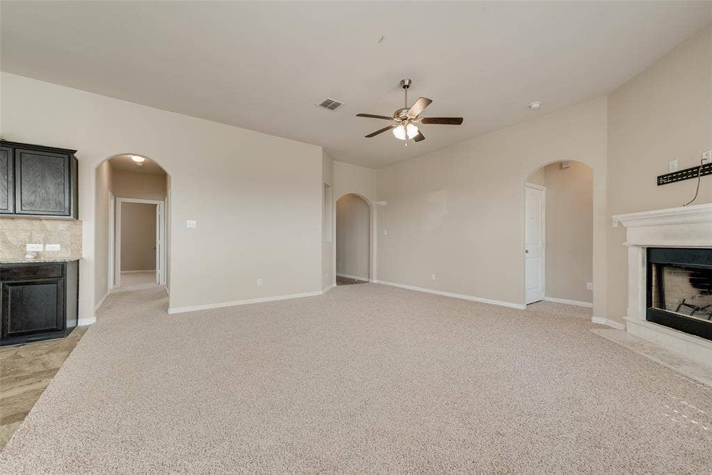 215 Fred Lane, Ferris, TX 75125 Recessed fireplace with a white mantel, ceiling fan with light fixture, arched doorways, and light-toned carpeting