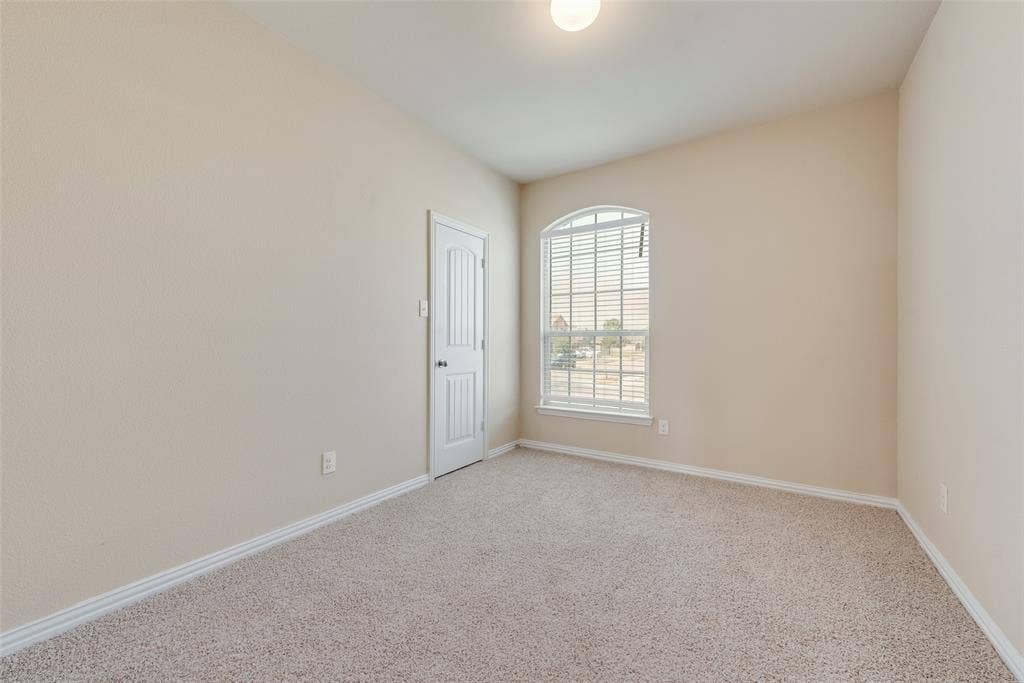 215 Fred Lane, Ferris, TX 75125 Arched window with blinds, vaulted ceiling, and neutral carpet flooring