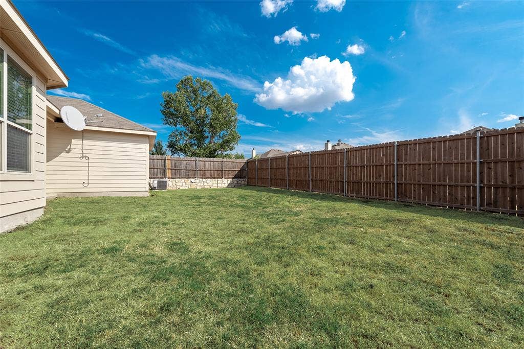 215 Fred Lane, Ferris, TX 75125 Expansive grassy yard with a privacy fence and stone retaining wall