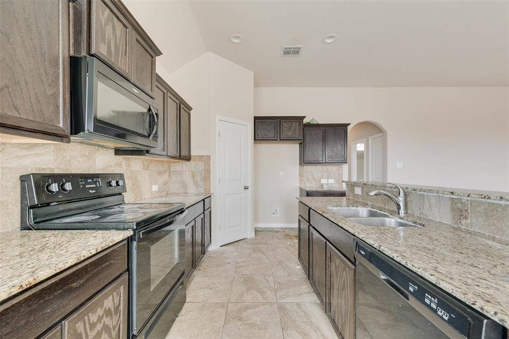 215 Fred Lane, Ferris, TX 75125 Kitchen featuring dark wood-finish cabinetry, granite countertops, tile backsplash, and a stainless steel double basin sink with a chrome faucet