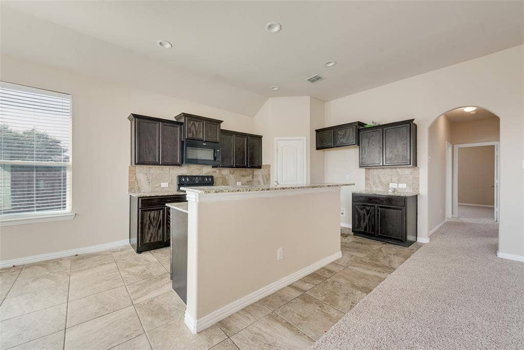 215 Fred Lane, Ferris, TX 75125 Kitchen area featuring dark wood-finish cabinetry, light-toned tiled flooring, recessed lighting, and a breakfast bar