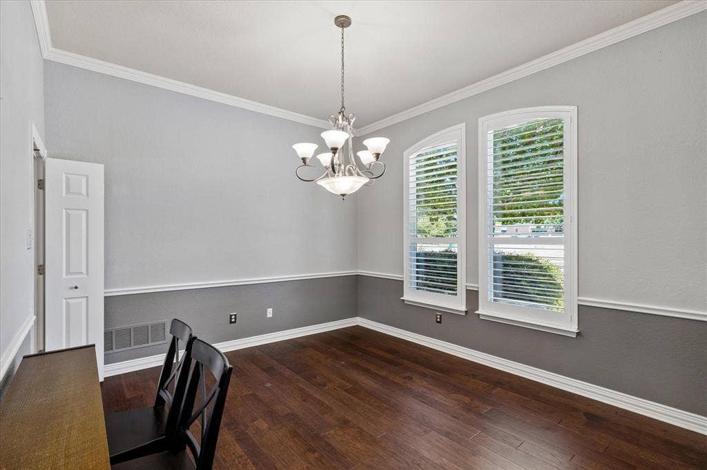 3800 Deer Forest Drive, Denton, TX 76208 Wood-finish flooring, two-tone wall treatment with chair rail, decorative crown molding, two arched windows with plantation shutters, and a five-light chandelier