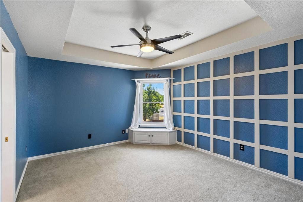 3800 Deer Forest Drive, Denton, TX 76208 Tray ceiling with a ceiling fan, accent wall with decorative paneling, built-in window bench, and wall-to-wall carpeting