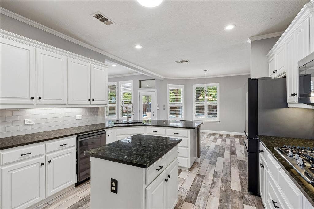 3800 Deer Forest Drive, Denton, TX 76208 White cabinetry, dark stone countertops, wood-finish flooring, stainless steel appliances, and a subway tile backsplash