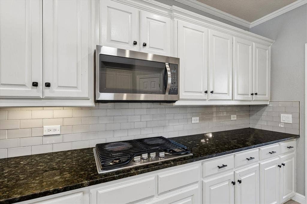 3800 Deer Forest Drive, Denton, TX 76208 White cabinetry, dark stone countertops, stainless steel microwave, gas cooktop, and subway tile backsplash