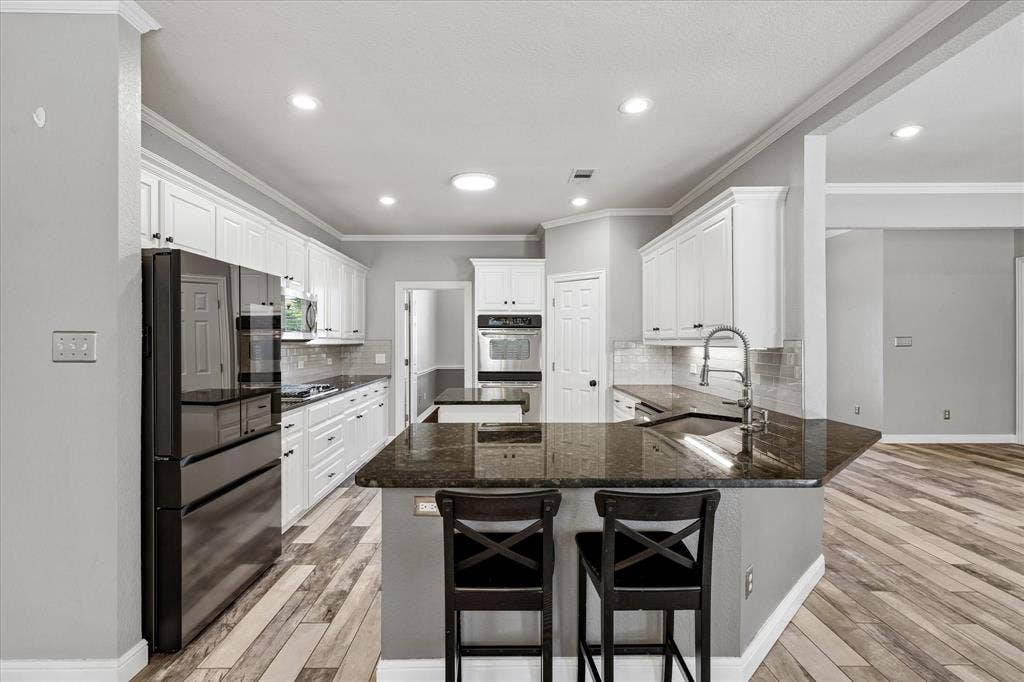 3800 Deer Forest Drive, Denton, TX 76208 Kitchen featuring wood-finish flooring, white cabinetry, dark countertops, a built-in oven, and a kitchen island with a sink