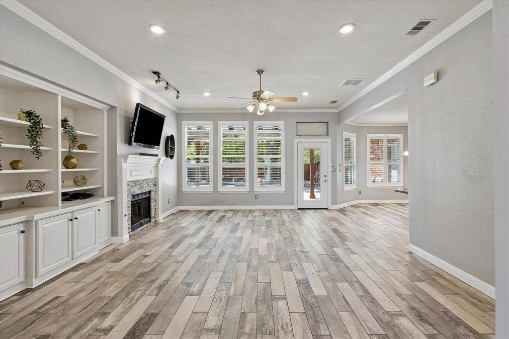 3800 Deer Forest Drive, Denton, TX 76208 Spacious living area featuring wood-finish flooring, a built-in shelving unit, and a stone-clad fireplace