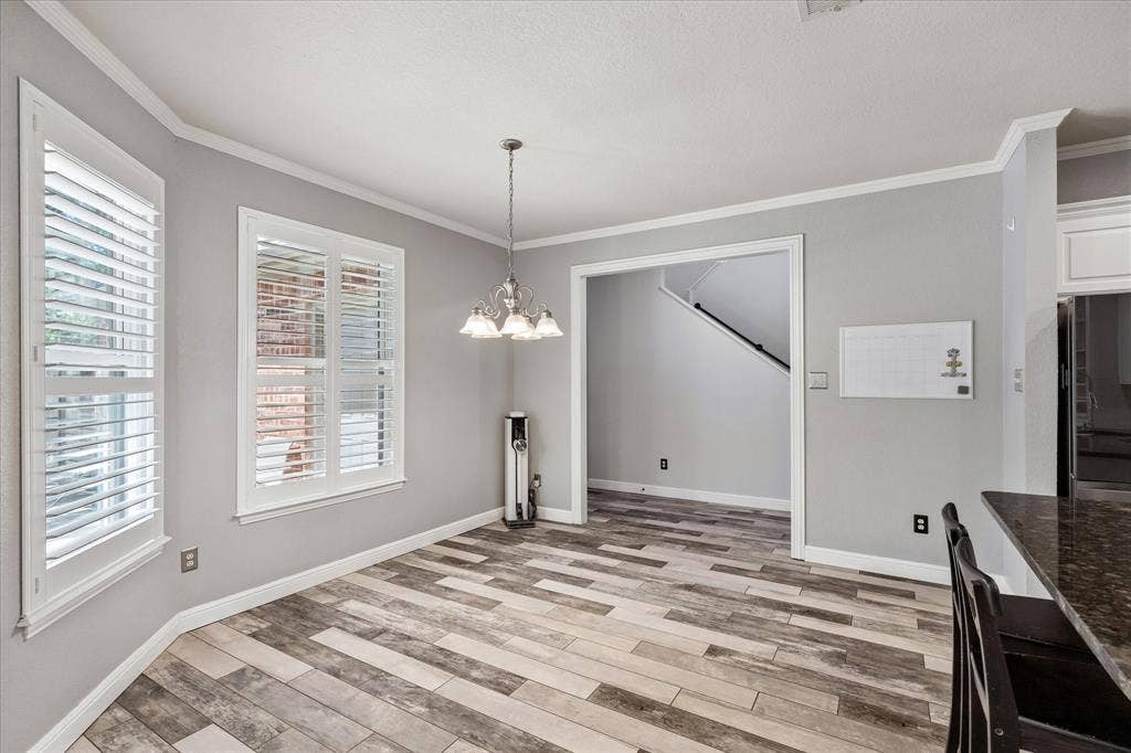3800 Deer Forest Drive, Denton, TX 76208 Wood-finish flooring, white plantation shutters, crown molding, and a chandelier illuminate this dining area