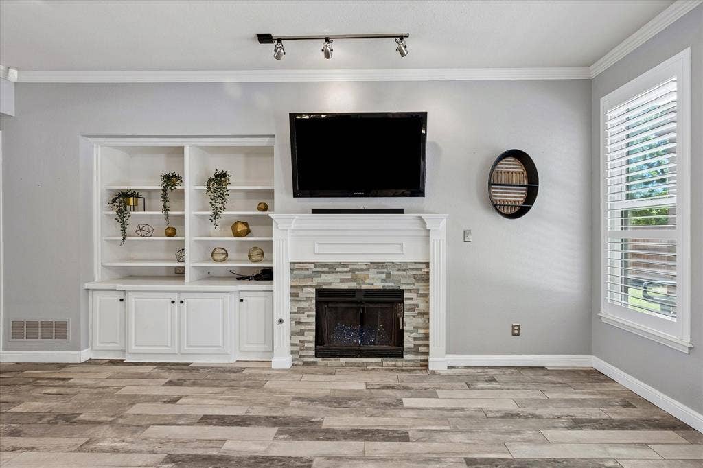 3800 Deer Forest Drive, Denton, TX 76208 Built-in shelving and cabinetry, fireplace with stone surround, crown molding, wood-finish flooring, and window with plantation shutters