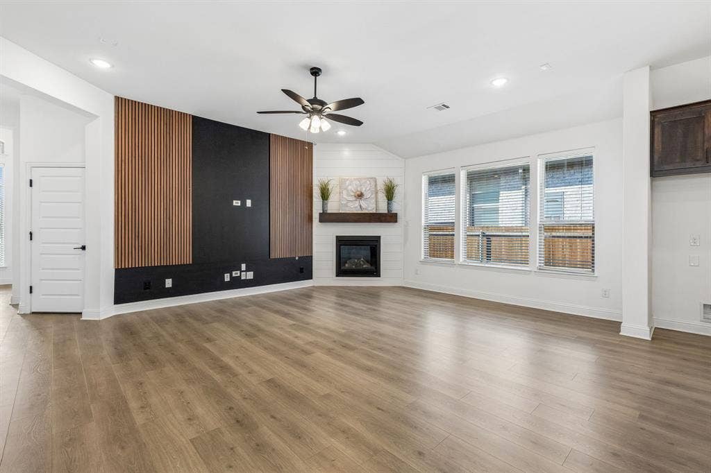 5224 Troupe Road, McKinney, TX 75071 Wood-finish flooring throughout, modern media wall with wood slat accents, corner fireplace with a wood mantle, white shiplap wall detail, and recessed lighting
