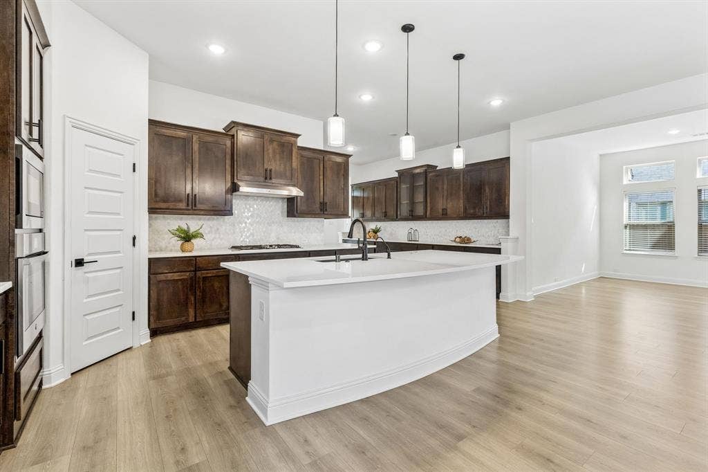 5224 Troupe Road, McKinney, TX 75071 Kitchen featuring dark wood cabinetry, white countertops, tile backsplash, built-in ovens, and a center island with sink