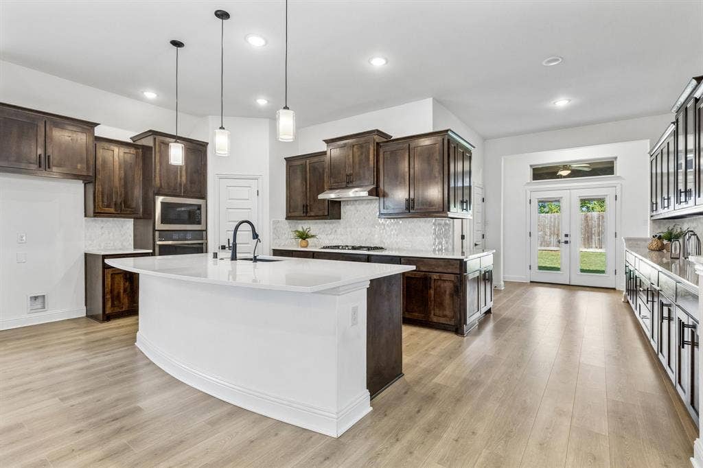 5224 Troupe Road, McKinney, TX 75071 Modern kitchen featuring a large central island with a solid surface countertop, dark wood-finish cabinetry, and light wood-finish flooring