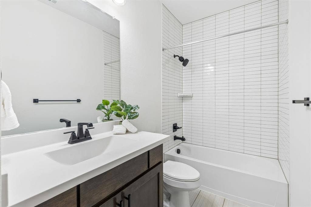 5224 Troupe Road, McKinney, TX 75071 Bathroom featuring a dark wood-finish vanity with a white countertop, matte black fixtures, a built-in tub with a shower, and horizontal white tile surround