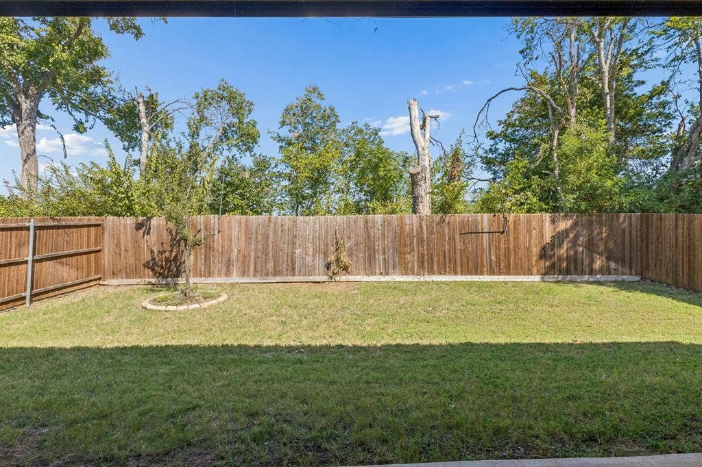 5224 Troupe Road, McKinney, TX 75071 Fenced backyard with a grassy lawn, mature perimeter trees, and a young tree with stone-edged landscaping