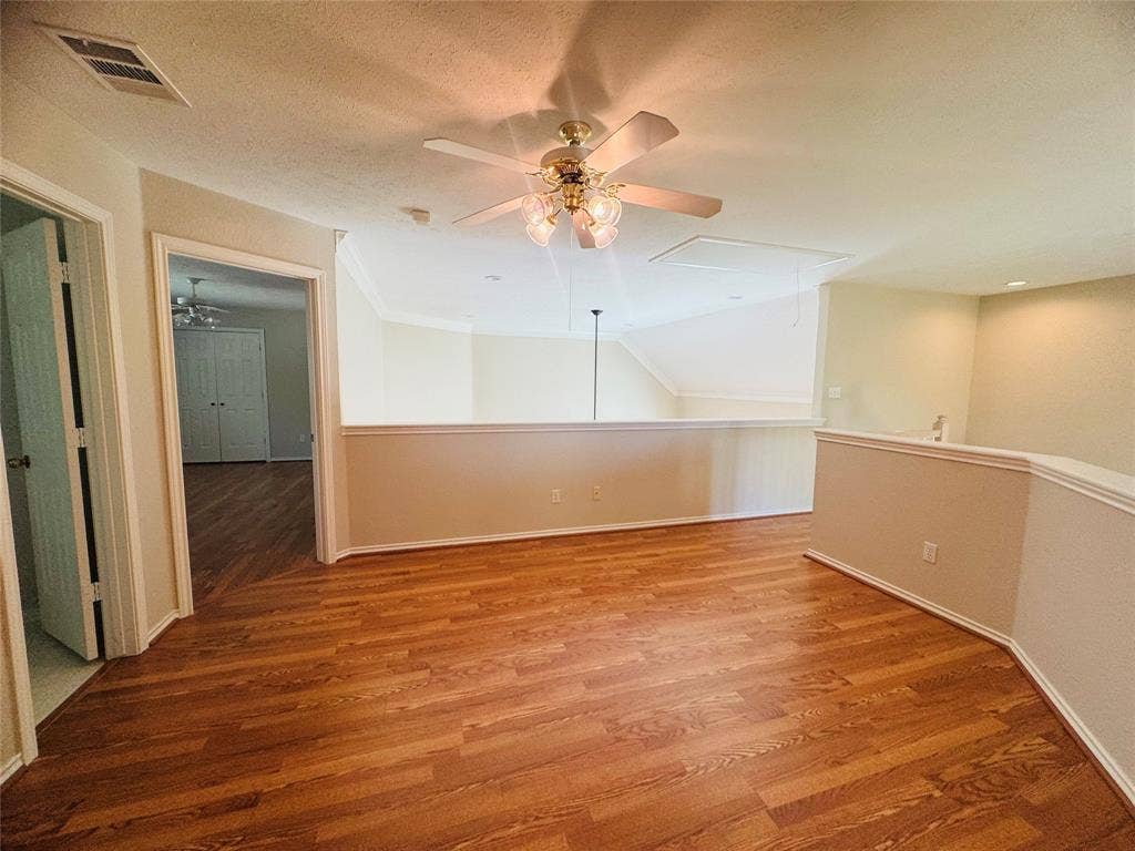 Wood-finish flooring throughout, ceiling fan with integrated lighting, and a half-wall balustrade with crown molding