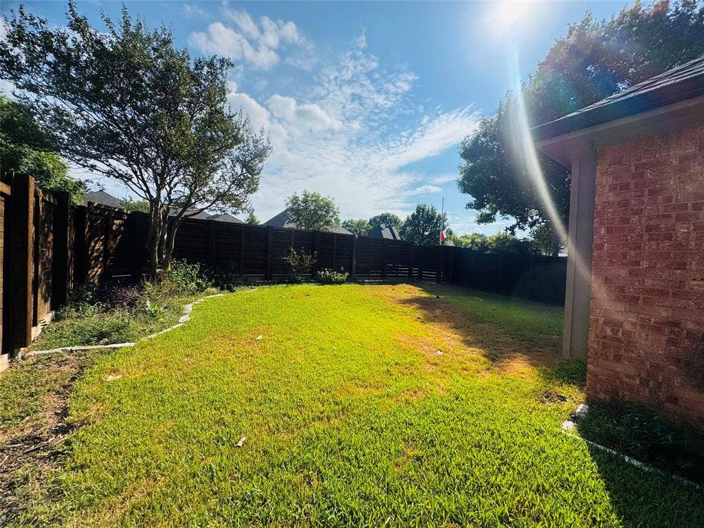 Expansive backyard featuring a manicured lawn, established trees, and perimeter fencing