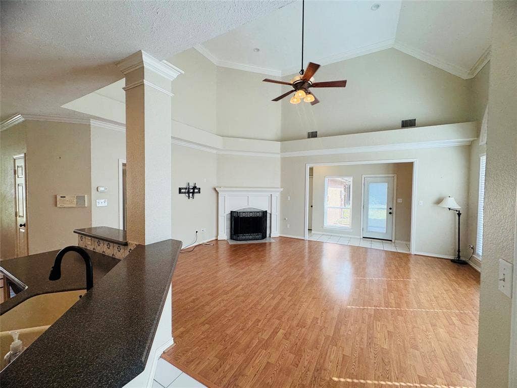 Vaulted ceiling with crown molding, wood-finish flooring, fireplace with white mantel, glass-paned exterior door, and built-in breakfast bar