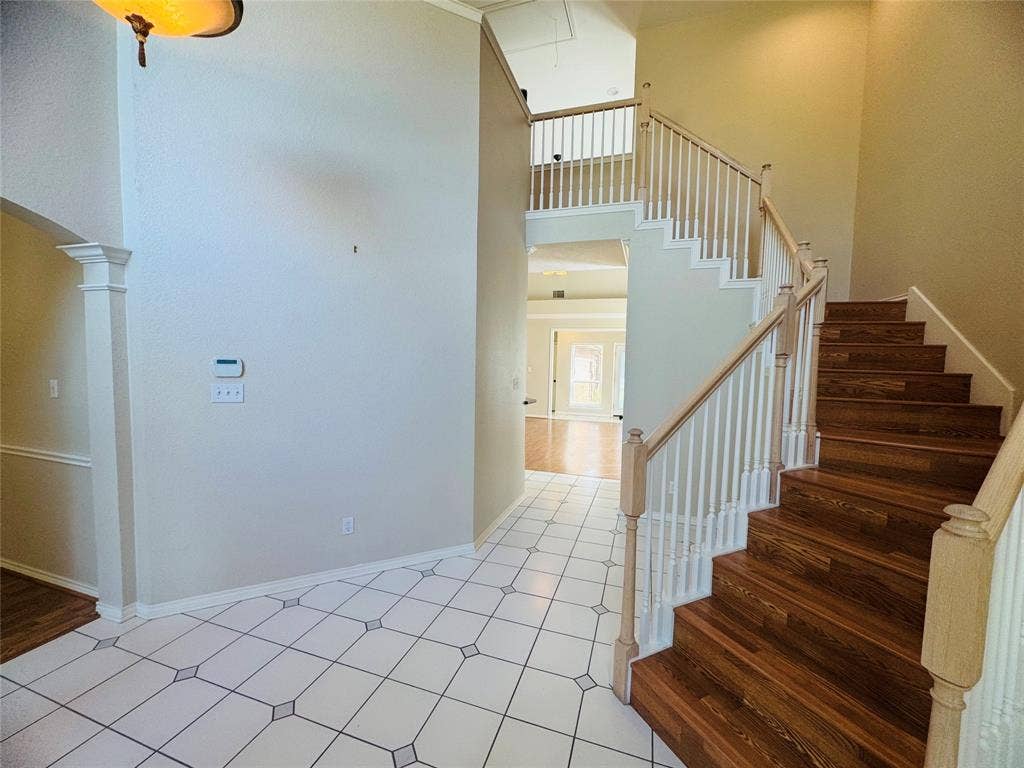 Two-story entryway featuring wood-finish staircase, white balusters, and square tile flooring with decorative inserts