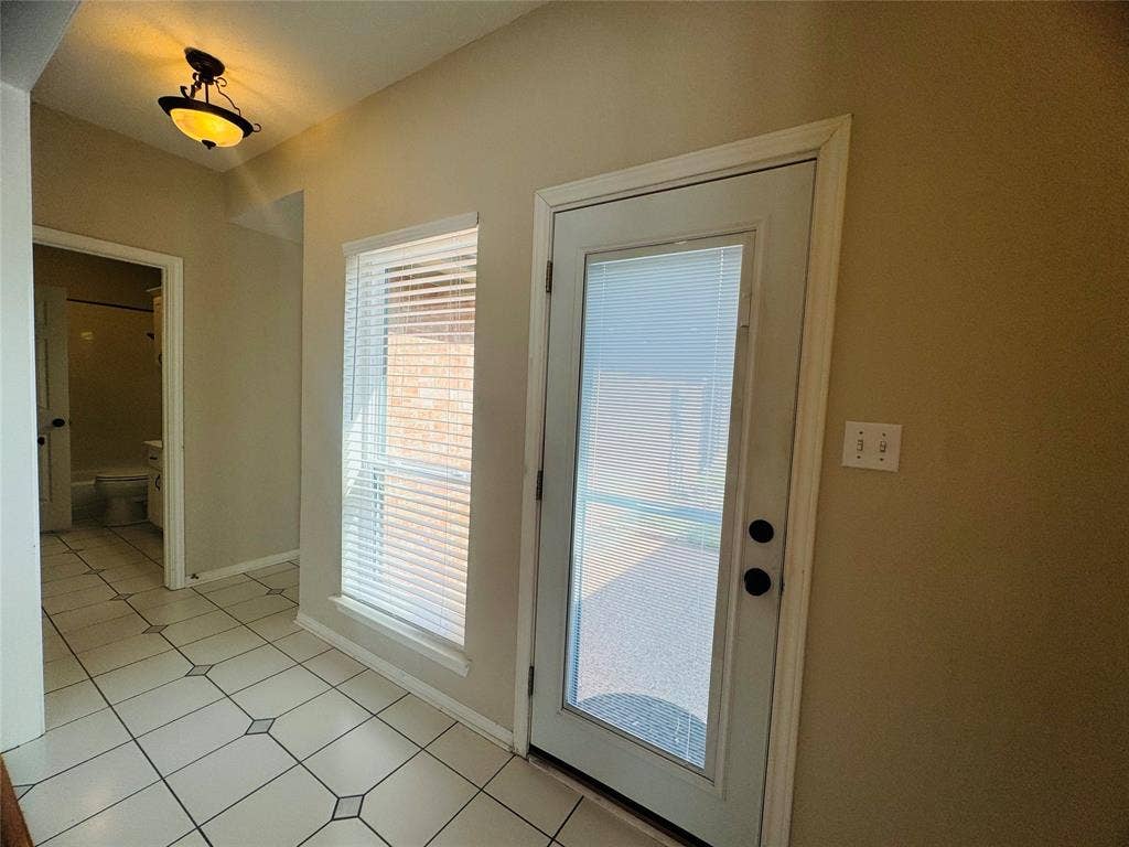 Tiled flooring with decorative accents, an exterior door with integrated blinds, and a large window with horizontal blinds