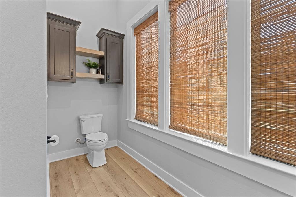 23180 Bridle View Drive, Lindale, TX 75771 Powder room featuring wood-finish flooring, three windows with woven blinds, and built-in cabinetry with open shelving